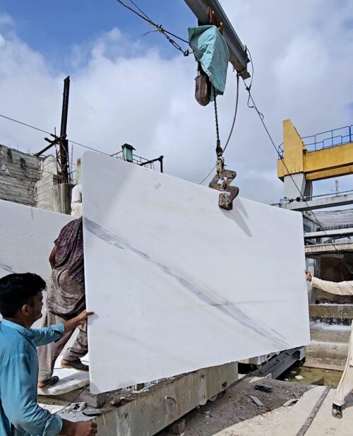White marble slab being lifted by crane at the stone yard